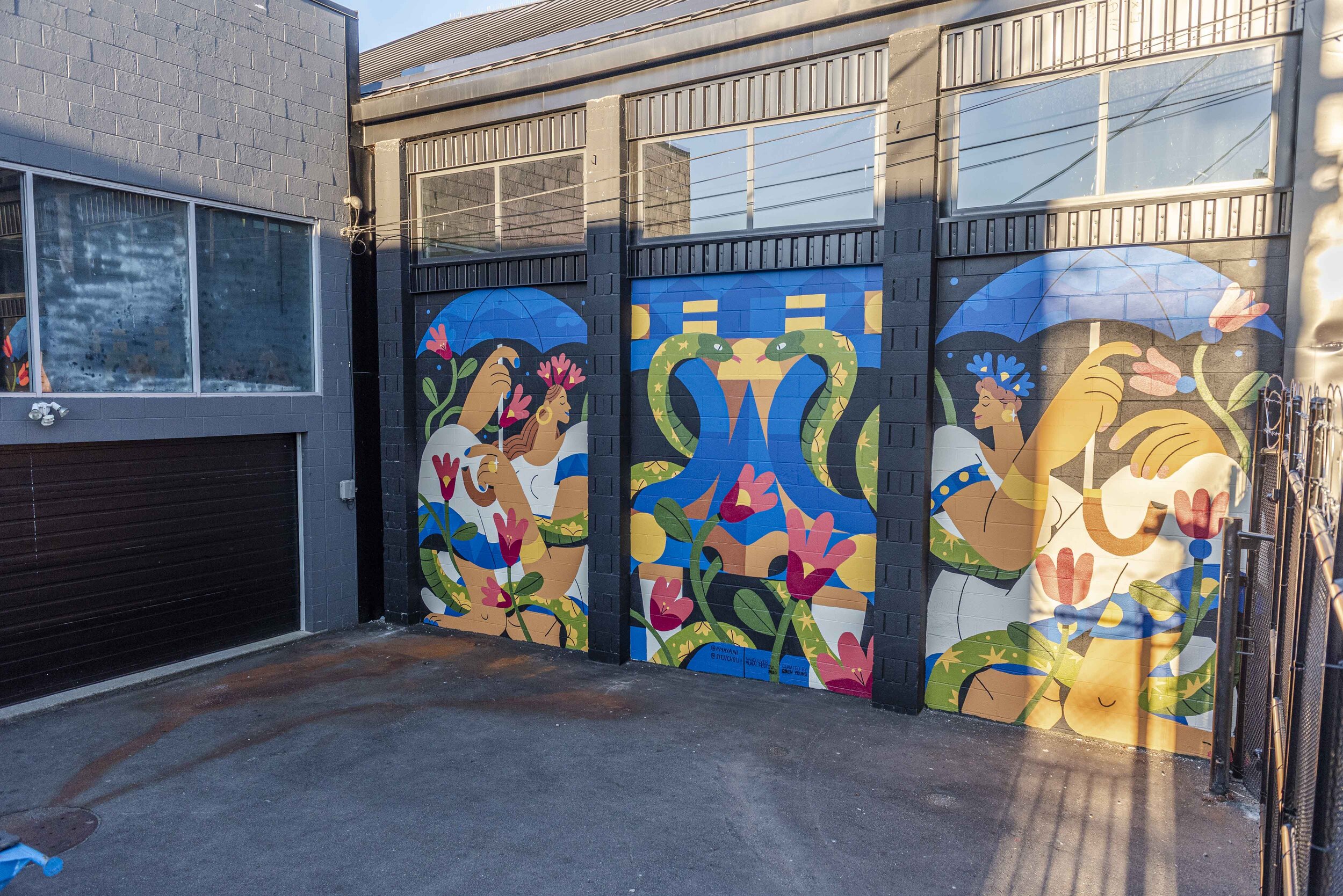Mural with three panels of women holding umbrellas and two snakes in a bed of flowers.