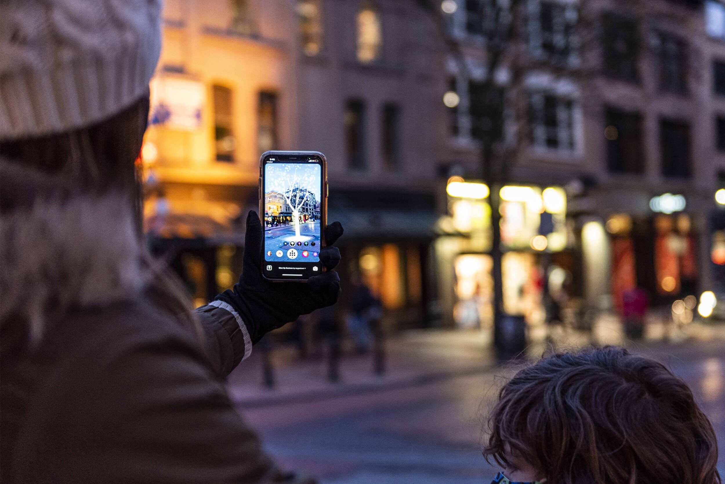 Person holding out phone in front of them looking at an Augmented Reality tree at night in Gastown, Vancouver