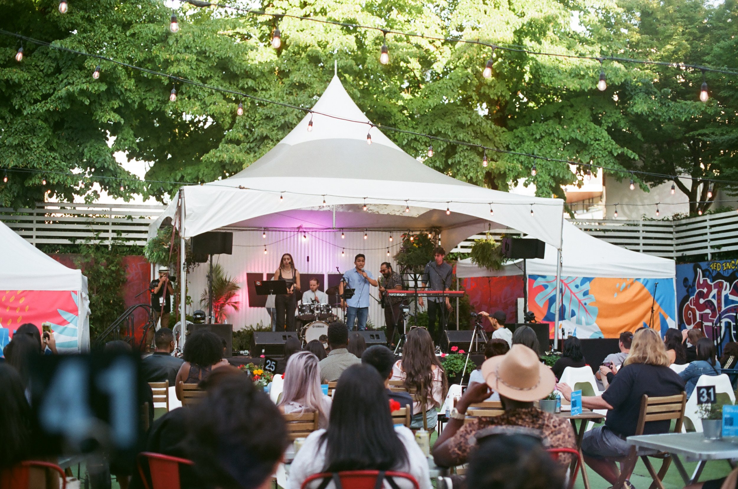band on stage under white tend with audience watching