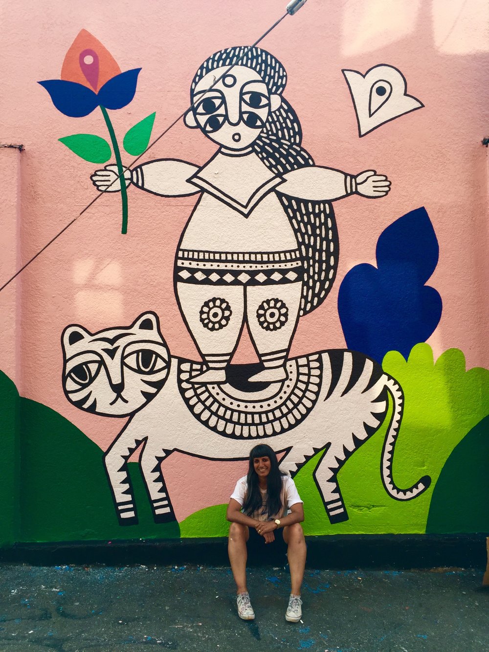 PHOTO CREDIT:  Megan Jenkins    Chats with Sandeep Johal @ Her mural: GIRLS ARE FIERCE LIKE TIGERS    I've lived in Mount Pleasant for over a decade. I currently live a few blocks away from my mural, which is located at a transit hub I use pretty consistently. To see it on an almost daily basis is pretty special.  It was important to me that the mural had a South Asian aesthetic to reflect my heritage. There are so few South Asian artists here (for many reasons, but the main one being artists aren't encouraged in my culture) and I wanted it to inspire other South Asians who are aspiring to work in the arts.&nbsp;The lady on the tiger originally came from a drawing I did at a residency at the Anvil Centre in New West last year.   Favourite things about painting the mural?&nbsp;   One of the best parts of painting this mural was meeting so many South Asians who came by to say hi and support me. I felt honoured to be painting a mural for VMF and scared, nervous about such a big wall, especially since it was my first outdoor mural. But, I did it, with the assistance from friends, and now all I want to do is paint murals all over the place — walls, ceilings, floors, stairs, wherever. I feel so much more confident. The press I got during the mural fest has also led to different opportunities and helped me propel my career forward, which I'm eternally thankful for.  The fact that VMF exists is a win. Supporting local talents, exposing the larger community to artists, giving everyone access to public art, and beautifying otherwise bland or under-utilized spaces is only some of what VMF is doing to make Vancity better. The fact that VMF is working towards 50% of the artists being female, supporting Indigenous artists, and first time muralists is pretty awesome. Oh, and the artists get paid! :)&nbsp;