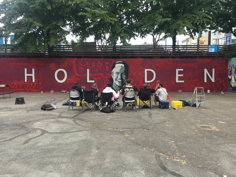 Reposted from Tara Maguire (Holden's Mother)'s  blog   .    I have no grave to place flowers by.&nbsp;&nbsp;  I have no headstone to polish and sweep.&nbsp;&nbsp;I do have a beautiful, smooth, wooden box, made by my husband Cam, that we keep on the same shelf as the vodka. We don’t reach for the vodka often, or the box for that matter. The box contains the burned bones of my son.  And now I also have a sixty-five foot cement wall in a parking lot in East Vancouver covered in glorious red paint, at the centre of which there is a huge and uncanny portrait of my son Holden in black and white, smiling out at the world.&nbsp;&nbsp;He looks truly happy.&nbsp;&nbsp;I hope it’s true. There is no good resting place for your child, but this wall makes sense. &nbsp; If there has to be a symbolic location for Holden to be recognized, well, this is his kind of place. &nbsp;  The background of the mural is covered in reproductions of Holden’s own graffiti lovingly re-created by some of his closest friends.&nbsp;&nbsp;There are imprints of some of his tattoos, tributes and secret messages. &nbsp;I hope you get the chance to see it up close. &nbsp;Watching those kids work so hard was a very emotional and powerful experience.&nbsp;&nbsp;It was a modern ritual of love and devotion.&nbsp;&nbsp;An urban salute and a glorious tribute to a fallen comrade. &nbsp;I am forever grateful for their beautiful work, their sincere efforts and their friendship of Holden. They honoured him in a way they couldn’t do in a church, or with a memorial service, &nbsp;a way that was intrinsically him. It was a &nbsp;precious gift to all of us.&nbsp;  I was &nbsp;moved over and over again on Saturday by the comments people made to me about how much Holden had impacted their lives with his kindness, his understanding and his unique charms. His actions have sent ripples into many many hearts. We all miss Holden and I think he misses us too. &nbsp;He would have thought the day was pretty cool.&nbsp;  “How long will it stay?” Someone asked me that day. &nbsp;&nbsp;  “I really can’t say.”&nbsp;  Maybe a year, until it gets painted over.&nbsp;&nbsp;Maybe longer.&nbsp;&nbsp;Maybe the whole wall will be torn down for development by Christmas.&nbsp;&nbsp;You know, retail on the bottom, condos up top.&nbsp;&nbsp;Maybe that’s why they offered the wall in the first place.&nbsp;&nbsp;Or maybe next week some little punk will scrawl a drunken tag over his gorgeous face. That would make me fume and it would also be quite fitting. The nature of street art is temporary.&nbsp;&nbsp;And so is the nature of life.  How long will you live?  “I really can’t say.”  When Holden passed away two summers ago a friend suggested starting some kind of legacy fund.&nbsp;&nbsp;In my sorrow, I had no idea what that meant.&nbsp;&nbsp;She placed papers in front of me and I signed them like a robot, &nbsp;with no intention other than doing what I thought I was supposed to do at the time.  “At times like this people want do to something to help,” I think she said.  “And you don’t want all that lasagne,” said another.  “Just get it started and you can decide later what to do with it.”  People are generous and people are kind and people gave and the  Holden Courage Memorial Fund for Artists  grew. This spring, on a day I did not feel like crying, I contacted the  Vancouver Mural Festival &nbsp;to see if they had any ideas about how to use the grant proceeds. The organizers offered to create a live graffiti jam in Holden’s honour which made me feel like crying in a completely different way.&nbsp;&nbsp;The whole festival was incredible. There are more than 50 stunning murals around the city.&nbsp;&nbsp;There are  tours every Saturday &nbsp;or just grab a map and walk around to find them. &nbsp;What a treasure on our streets.  Holden loved graffiti. He loved everything about it. The creativity, the smell, the camaraderie, the rebellion, the music, the danger, the colour, the risks and the thrill. &nbsp;He may even have enjoyed getting arrested for it, as a badge of honour. &nbsp;From the time he was about eleven he drew and drew and drew and drew those tags. His work evolved and changed and grew more intricate but it never ever stopped.&nbsp;&nbsp;Until it did.  On Saturday, at the Holden Courage Memorial Graffiti Jam, I got the chance to use a little bit of spray paint.&nbsp;&nbsp;As I stood there, in front of the wall, shaking that can and feeling the thump of the metal balls inside stirring the paint, I felt like a total badass.&nbsp;&nbsp;A middle aged, motherly badass, but a badass none-the-less.&nbsp;&nbsp;In that moment I think I understood a little bit of how Holden may have felt when he painted.&nbsp;  Free and alive, brave and unlimited.&nbsp;  With much love and deep gratitude,  ~ tara  **&nbsp;If you would like to see the memorial wall, it is at East 5th Avenue and Main, on the NW corner, in the parking lot. &nbsp;All contributions to  The Holden Courage Memorial Fund for Artists &nbsp;are gratefully accepted. We have a few photo books of Holden’s graffiti work left.&nbsp;&nbsp;If you would like one, please let me know and I will get one to you.&nbsp;We ask for a minimum $20 donation.&nbsp;&nbsp;We are hoping that we can support other talented artists in creating more beauty on the walls of Vancouver. &nbsp;Because what made Holden truly happy was putting paint on walls. &nbsp;Thank you!**